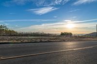 the sun rises over a small mountain on a highway that goes into the distance as a horse is standing in the foreground