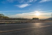 the sun rises over a small mountain on a highway that goes into the distance as a horse is standing in the foreground