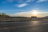 the sun rises over a small mountain on a highway that goes into the distance as a horse is standing in the foreground