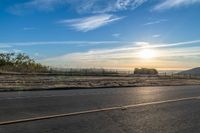 the sun rises over a small mountain on a highway that goes into the distance as a horse is standing in the foreground