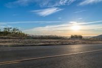 the sun rises over a small mountain on a highway that goes into the distance as a horse is standing in the foreground