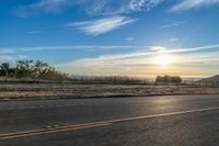 the sun rises over a small mountain on a highway that goes into the distance as a horse is standing in the foreground