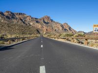 the desert road and mountains are empty of cars and a sign points out where to go