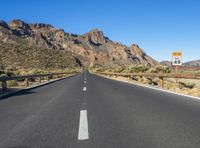 the desert road and mountains are empty of cars and a sign points out where to go