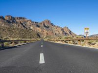 the desert road and mountains are empty of cars and a sign points out where to go