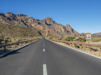 the desert road and mountains are empty of cars and a sign points out where to go