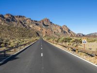 the desert road and mountains are empty of cars and a sign points out where to go