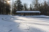 a pavilion on a snowy day in a park area with tracks of snow covered grass