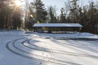 a pavilion on a snowy day in a park area with tracks of snow covered grass