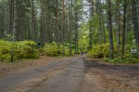 a man rides a bike down a dirt road in the forest while some people stand nearby