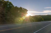 an image of the sun behind the road with trees on both sides and two roads