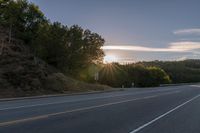 an image of the sun behind the road with trees on both sides and two roads