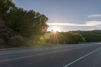 an image of the sun behind the road with trees on both sides and two roads