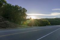 an image of the sun behind the road with trees on both sides and two roads