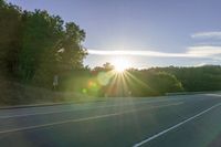 an image of the sun behind the road with trees on both sides and two roads