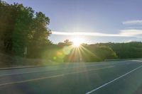 an image of the sun behind the road with trees on both sides and two roads