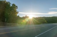 an image of the sun behind the road with trees on both sides and two roads