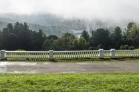 an empty park bench next to a large grassy field and mountains in the background with clouds