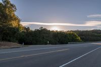 the sun is setting in the distance behind trees on the highway that goes from sunset to sunset