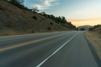 a curve on a mountain highway at sunset with a single car going around it and it's front end