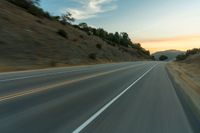 a curve on a mountain highway at sunset with a single car going around it and it's front end