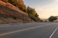 a lone motorcycle is driving down a rural road, at dusk, and the sun sets