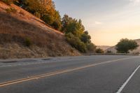 a lone motorcycle is driving down a rural road, at dusk, and the sun sets