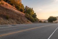 a lone motorcycle is driving down a rural road, at dusk, and the sun sets