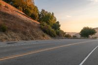 a lone motorcycle is driving down a rural road, at dusk, and the sun sets