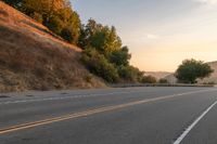 a lone motorcycle is driving down a rural road, at dusk, and the sun sets