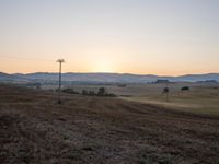 a hill is pictured with sunset on the horizon and power lines in the foreground