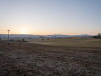 a hill is pictured with sunset on the horizon and power lines in the foreground