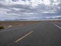 a road in a desert with mountains on both sides of it and clouds overhead and an area full of arid land below