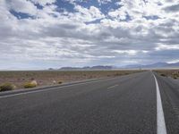 a road in a desert with mountains on both sides of it and clouds overhead and an area full of arid land below