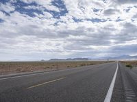 a road in a desert with mountains on both sides of it and clouds overhead and an area full of arid land below