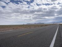 a road in a desert with mountains on both sides of it and clouds overhead and an area full of arid land below