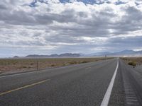 a road in a desert with mountains on both sides of it and clouds overhead and an area full of arid land below