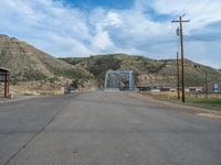 an empty street and a metal bridge on a hill in the distance, near the buildings