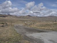 there is a grassy field with hills in the background and an empty road on the ground