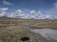 there is a grassy field with hills in the background and an empty road on the ground