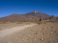 a view of a volcano with sparse rocks on the ground with a dirt path leading to it