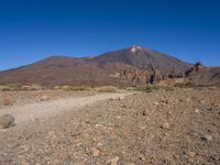 a view of a volcano with sparse rocks on the ground with a dirt path leading to it