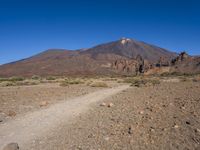 a view of a volcano with sparse rocks on the ground with a dirt path leading to it