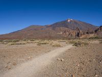 a view of a volcano with sparse rocks on the ground with a dirt path leading to it