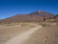 a view of a volcano with sparse rocks on the ground with a dirt path leading to it