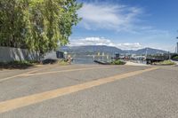 a street with a boat dock and a house next to it and water in the background