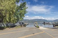 a street with a boat dock and a house next to it and water in the background