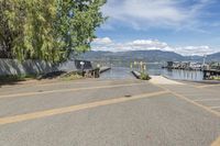 a street with a boat dock and a house next to it and water in the background