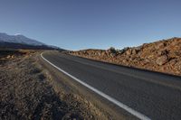 a very long empty road on a snowy mountain range with a snow covered peak in the distance