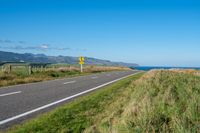 a paved road leading to the ocean on a sunny day and a hill behind it